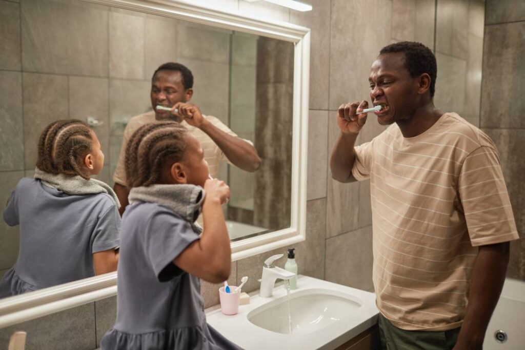 Father and daughter looking at one another while brushing teeth