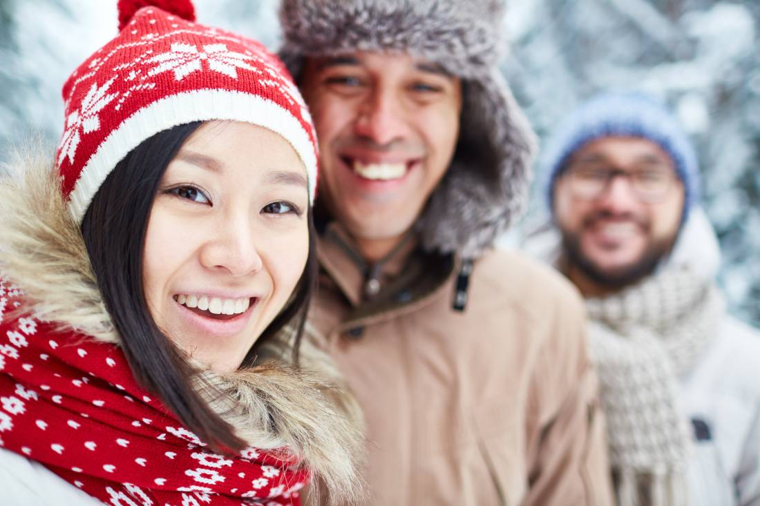 Three people flash beautiful smiles while in their winter gear in the snow outdoors